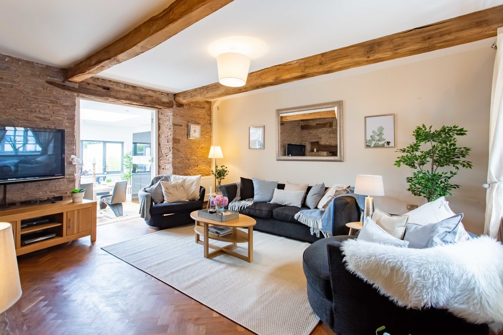 Idee per un soggiorno country con pareti beige, pavimento in legno massello medio, TV a parete e pavimento marrone