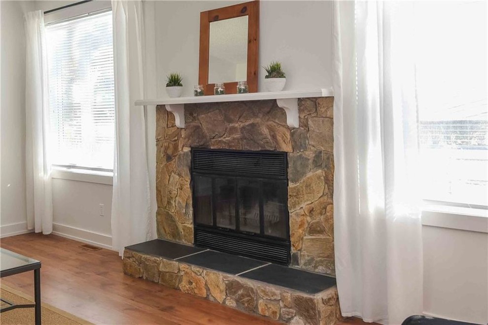 バンクーバーにある低価格の中くらいなトラディショナルスタイルのおしゃれな独立型リビング (白い壁、ラミネートの床、標準型暖炉、石材の暖炉まわり、テレビなし、茶色い床) の写真