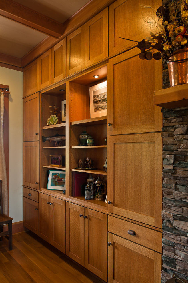 Cette photo montre un grand salon craftsman ouvert avec un mur beige, un sol en bois brun, une cheminée standard, un manteau de cheminée en pierre et un téléviseur encastré.