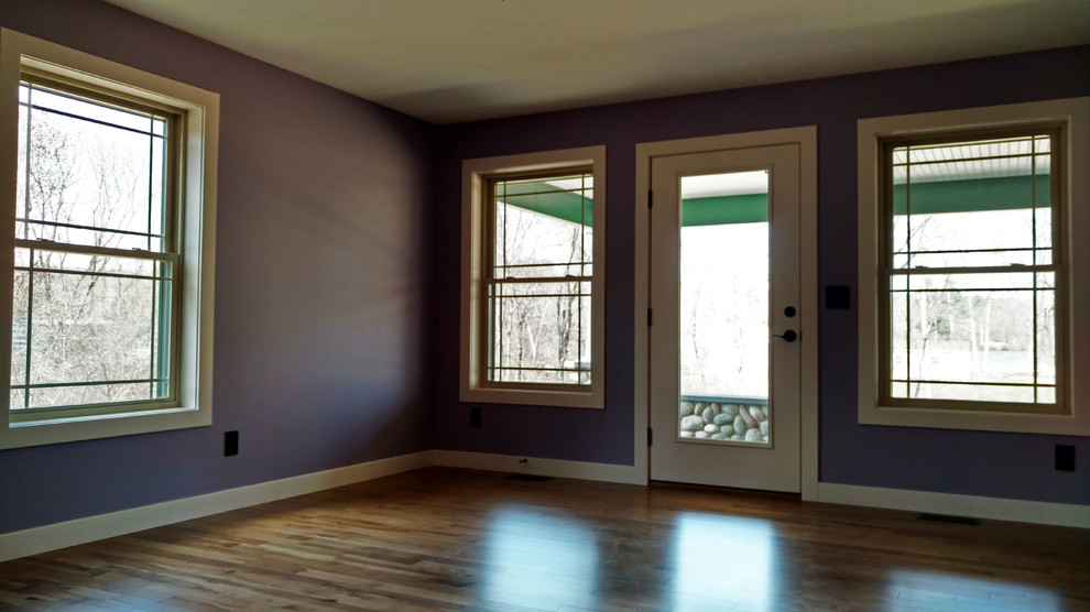 Diseño de salón cerrado de estilo americano con paredes púrpuras, suelo de madera en tonos medios y suelo marrón
