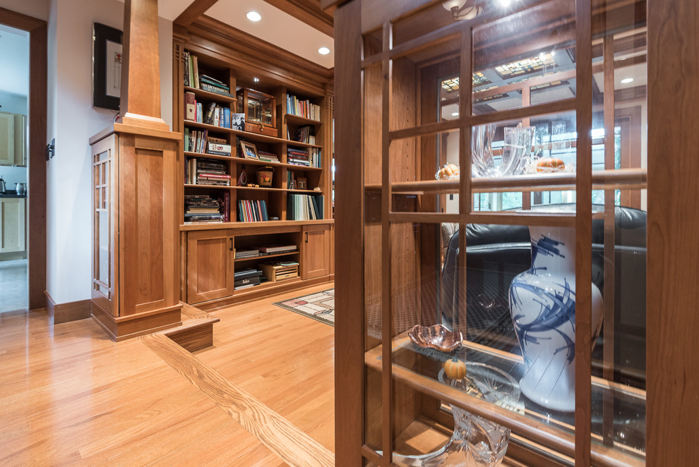 Imagen de biblioteca en casa abierta de estilo americano grande sin chimenea y televisor con paredes beige y suelo de madera clara