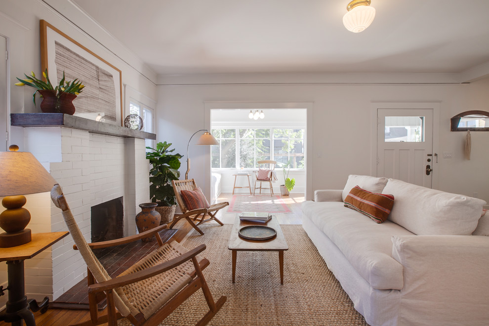 На фото: гостиная комната в морском стиле с белыми стенами, паркетным полом среднего тона, стандартным камином, фасадом камина из кирпича и коричневым полом