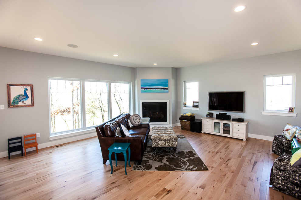 Foto de salón abierto de estilo americano grande con paredes grises, suelo de madera clara, chimenea de esquina y televisor colgado en la pared