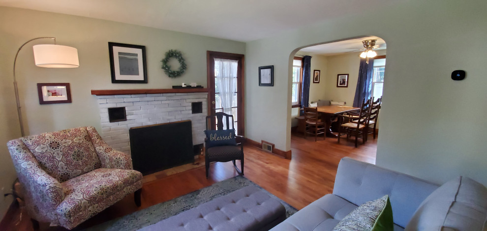 Cette image montre un salon traditionnel de taille moyenne et ouvert avec un mur vert, un sol en bois brun, une cheminée standard, un manteau de cheminée en brique et un téléviseur fixé au mur.