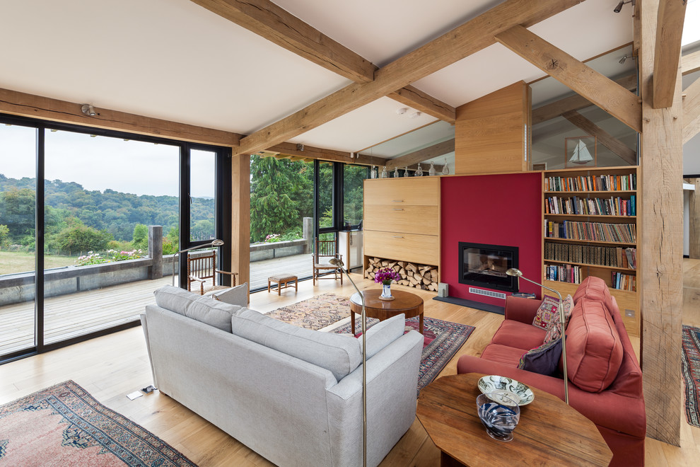 Ejemplo de biblioteca en casa abierta actual con paredes rojas, suelo de madera clara y chimenea de doble cara