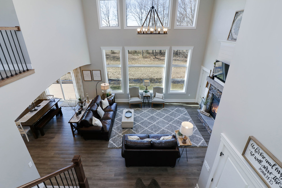 Cette photo montre un grand salon nature ouvert avec une salle de réception, un mur gris, un sol en bois brun, une cheminée standard, un manteau de cheminée en pierre, un téléviseur fixé au mur et un sol marron.
