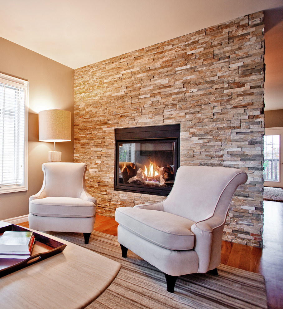 Idée de décoration pour un salon tradition ouvert avec un sol en bois brun, une cheminée standard, un manteau de cheminée en pierre et un mur gris.