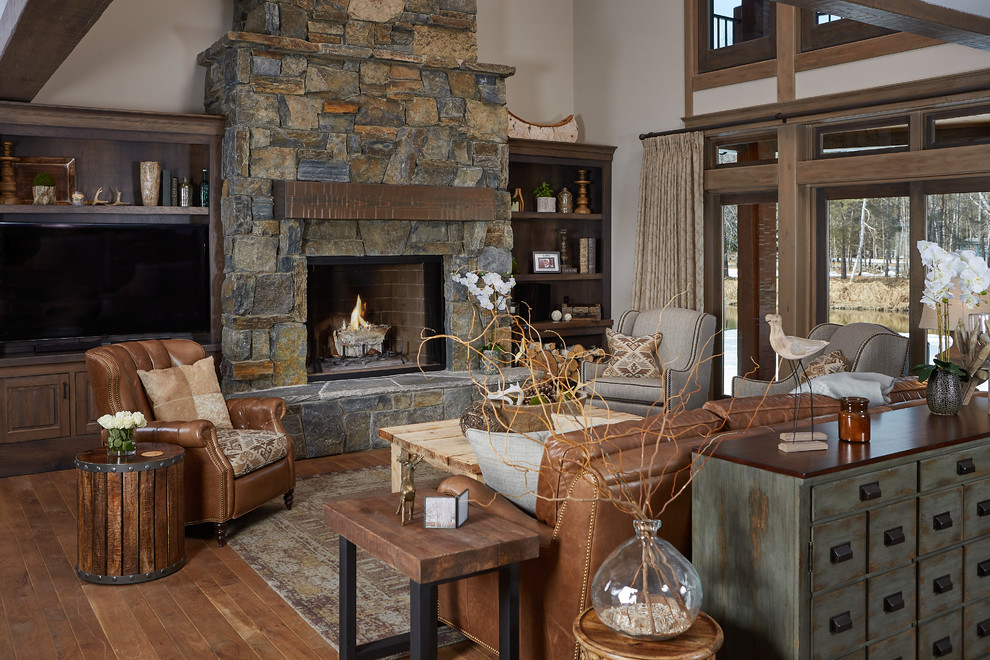 This is an example of a rustic open plan living room in Grand Rapids with brown walls, medium hardwood flooring, a standard fireplace, a stone fireplace surround and a built-in media unit.