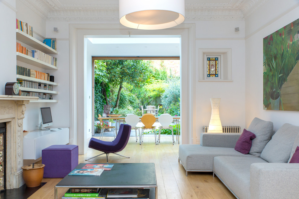 Immagine di un soggiorno design chiuso con libreria, pareti bianche, parquet chiaro e camino classico