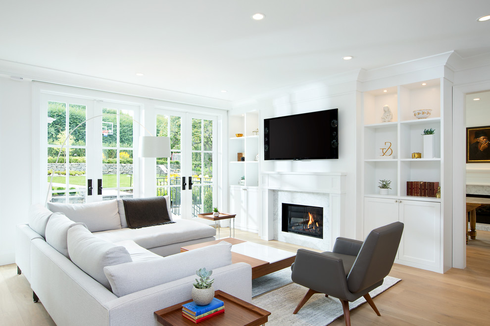 Immagine di un soggiorno chic con pareti bianche, pavimento in legno massello medio, camino classico e TV a parete