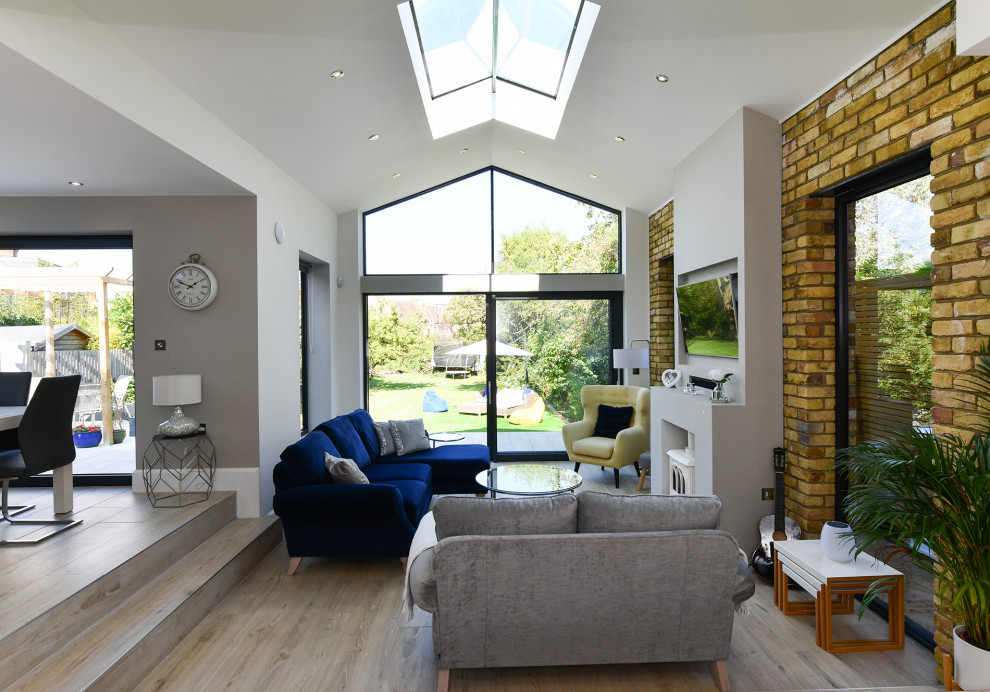 Photo of a medium sized contemporary open plan living room in London with a wood burning stove, a plastered fireplace surround, a wall mounted tv and a vaulted ceiling.