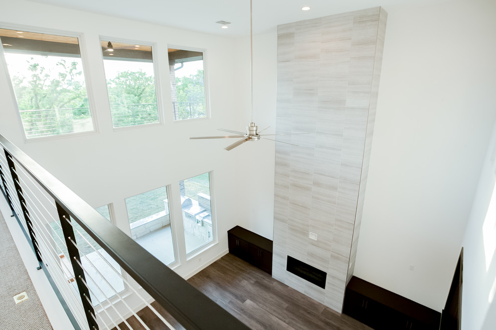 Пример оригинального дизайна: большая открытая гостиная комната в стиле модернизм с белыми стенами, паркетным полом среднего тона, горизонтальным камином, фасадом камина из плитки, телевизором на стене и коричневым полом