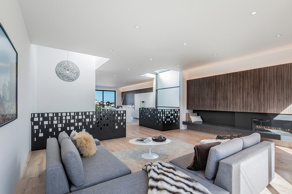 Ejemplo de salón abierto escandinavo grande con paredes blancas, suelo de madera clara, chimenea lineal, marco de chimenea de metal y televisor retractable