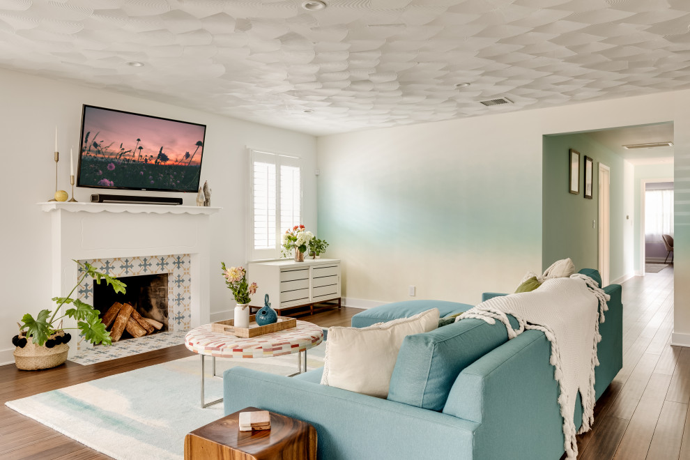 Пример оригинального дизайна: гостиная комната в стиле неоклассика (современная классика) с разноцветными стенами, темным паркетным полом, стандартным камином, фасадом камина из плитки, телевизором на стене, коричневым полом и синим диваном