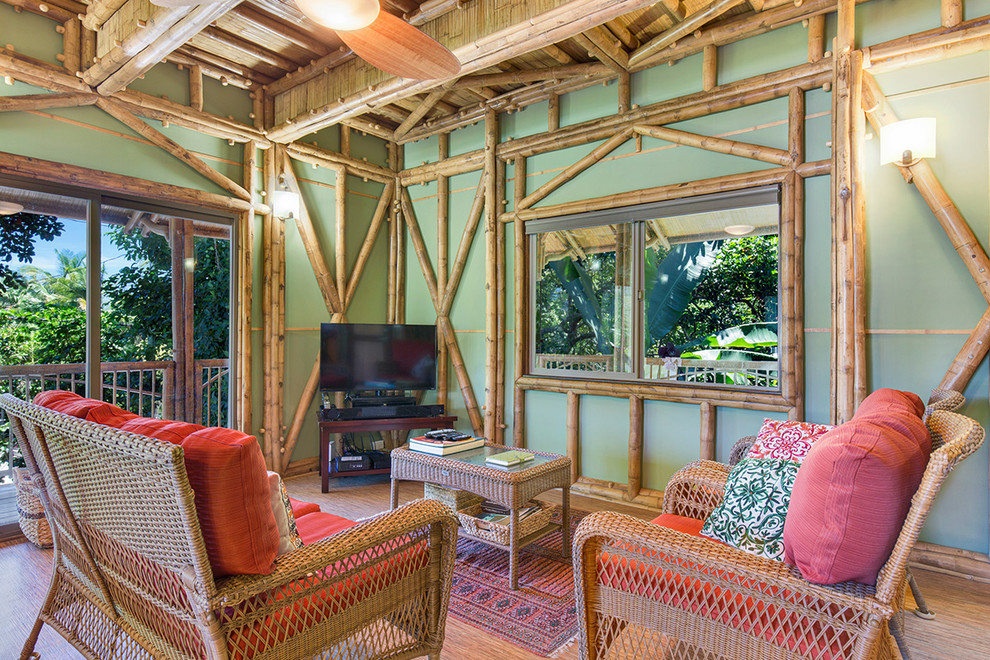 На фото: открытая гостиная комната в морском стиле с зелеными стенами, полом из бамбука и отдельно стоящим телевизором с