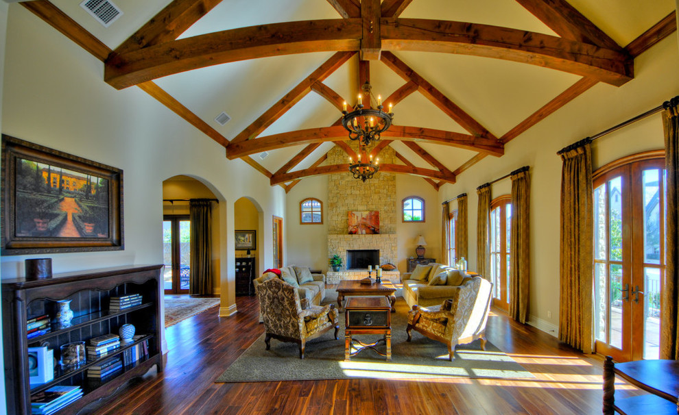 Imagen de salón abierto rural grande con paredes beige, suelo de madera en tonos medios, todas las chimeneas y marco de chimenea de piedra