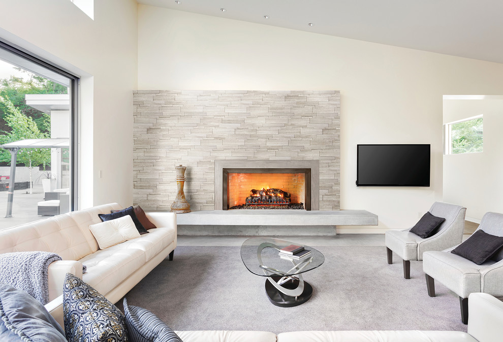 Источник вдохновения для домашнего уюта: большая открытая гостиная комната в современном стиле с белыми стенами, стандартным камином, фасадом камина из плитки, телевизором на стене и серым полом