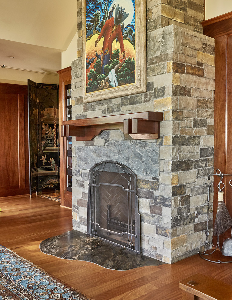 Aménagement d'un salon craftsman ouvert avec un sol en bois brun, une cheminée standard et un manteau de cheminée en pierre.
