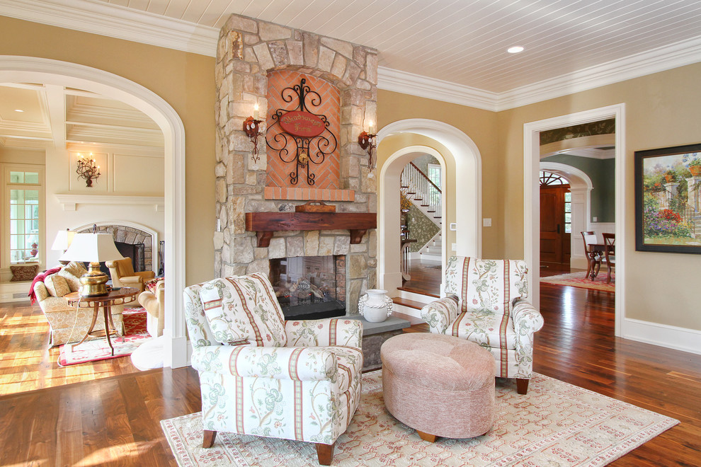 Imagen de salón abierto clásico con paredes beige, suelo de madera en tonos medios, todas las chimeneas y marco de chimenea de piedra