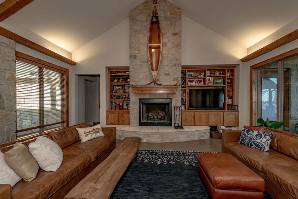 オースティンにある高級な中くらいなサンタフェスタイルのおしゃれなLDK (白い壁、コンクリートの床、標準型暖炉、石材の暖炉まわり、テレビなし、グレーの床) の写真