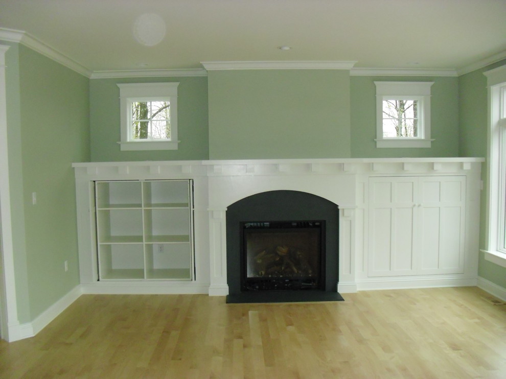 Modelo de salón cerrado de estilo americano de tamaño medio con paredes verdes, suelo de madera clara, todas las chimeneas y marco de chimenea de madera