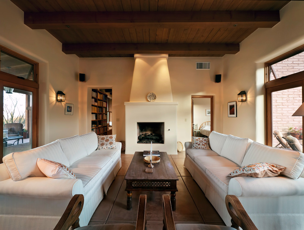 Cette image montre un salon sud-ouest américain fermé avec un mur blanc, sol en béton ciré, une cheminée standard, un manteau de cheminée en béton, un sol marron et poutres apparentes.