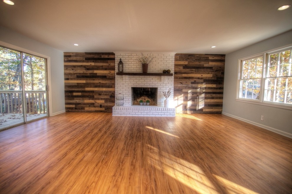 Cette photo montre un grand salon chic ouvert avec un mur gris, un sol en bois brun, une cheminée standard, un manteau de cheminée en brique, aucun téléviseur et un sol marron.