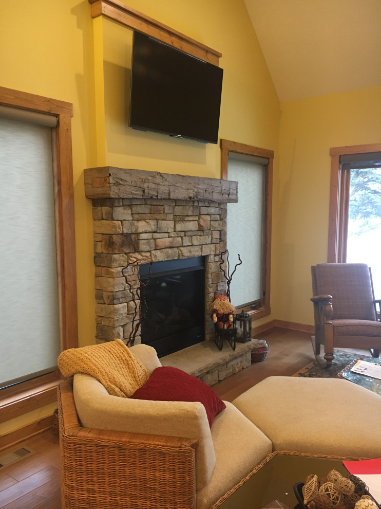 Mittelgroßes, Offenes Uriges Wohnzimmer mit gelber Wandfarbe, braunem Holzboden, Kamin, Kaminumrandung aus Stein und TV-Wand in Milwaukee