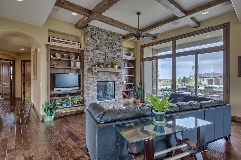 Inspiration for a mid-sized rustic open concept dark wood floor and brown floor living room remodel in Denver with a standard fireplace, a stone fireplace, a media wall and beige walls
