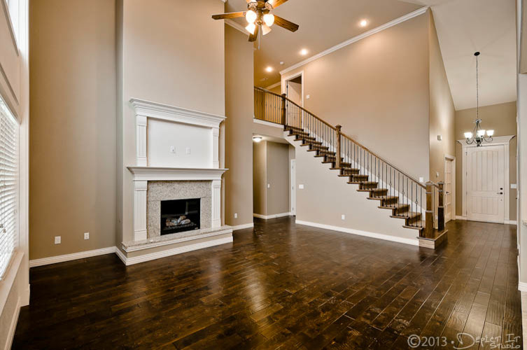 Offenes Klassisches Wohnzimmer mit beiger Wandfarbe, braunem Holzboden, Kamin, Kaminumrandung aus Stein und TV-Wand in Sonstige