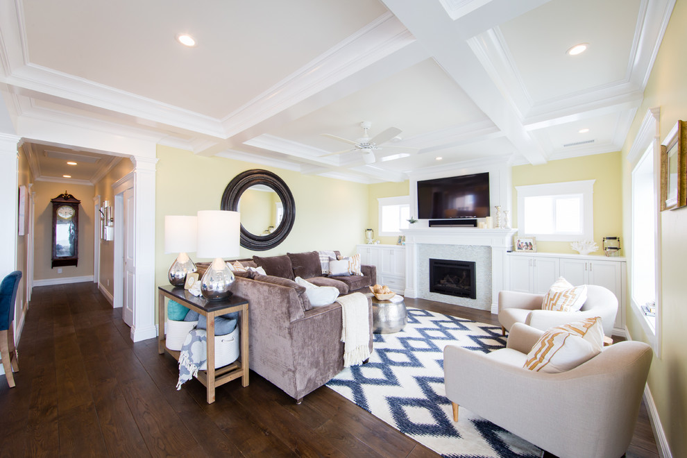 Стильный дизайн: гостиная комната среднего размера в морском стиле с желтыми стенами, паркетным полом среднего тона, стандартным камином, фасадом камина из плитки и телевизором на стене - последний тренд