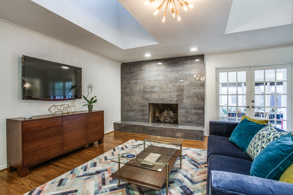 Idée de décoration pour un salon vintage avec un mur blanc, un sol en bois brun, une cheminée standard, un téléviseur fixé au mur et un sol marron.