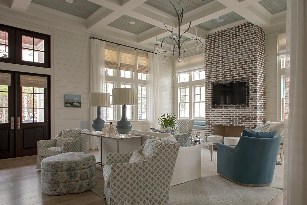 This is an example of a large beach style formal open plan living room in Other with white walls, medium hardwood flooring, a standard fireplace, a brick fireplace surround, a wall mounted tv and brown floors.