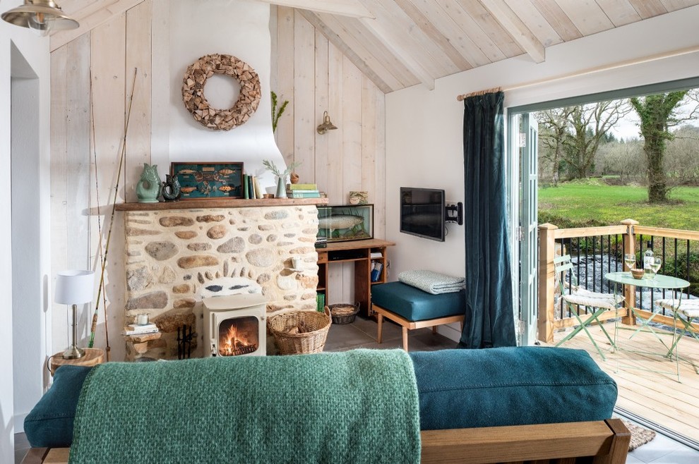 Country grey and teal living room in Cornwall with white walls, a wood burning stove, a stone fireplace surround and grey floors.