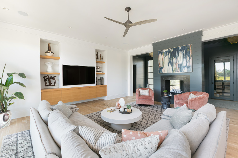 Imagen de salón actual con paredes blancas, suelo de madera clara, chimenea de doble cara, televisor colgado en la pared y suelo beige