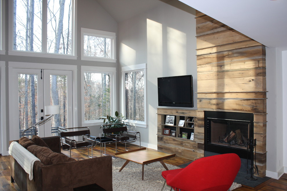 Modelo de salón para visitas tipo loft de estilo de casa de campo de tamaño medio con paredes grises, suelo de madera en tonos medios, todas las chimeneas, marco de chimenea de madera y televisor colgado en la pared
