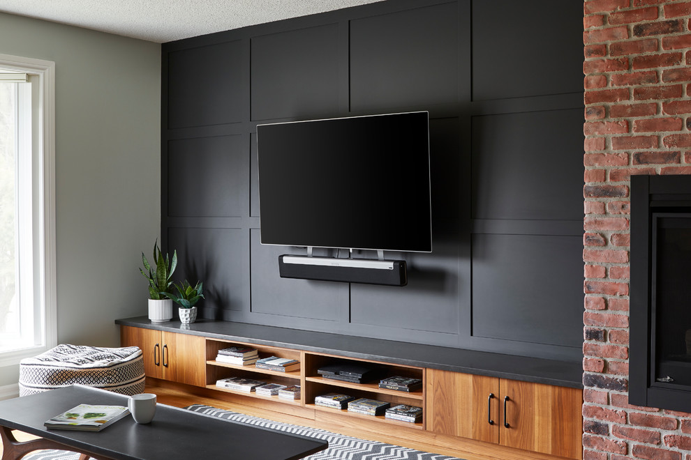 На фото: двухуровневая гостиная комната среднего размера в стиле ретро с серыми стенами, светлым паркетным полом, стандартным камином, фасадом камина из кирпича, телевизором на стене и коричневым полом с