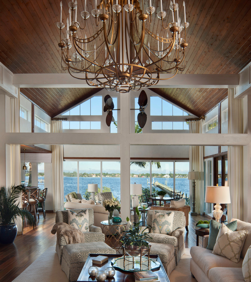 Modelo de salón abierto tropical grande sin chimenea con paredes blancas, suelo de madera en tonos medios y suelo marrón