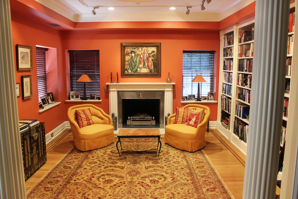 Immagine di un piccolo soggiorno tradizionale chiuso con libreria, pareti arancioni, parquet chiaro, camino classico, cornice del camino in metallo e nessuna TV