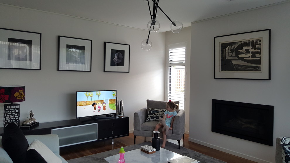 This is an example of a large modern living room in Sydney with white walls, medium hardwood floors, a hanging fireplace, a metal fireplace surround and a freestanding tv.