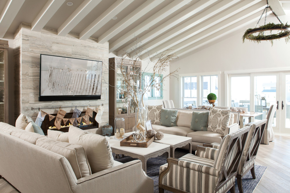 Diseño de salón abierto marinero grande con paredes blancas, suelo de madera clara, todas las chimeneas y televisor colgado en la pared
