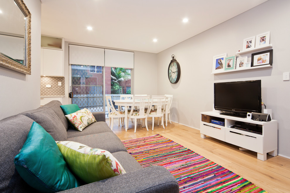 Small modern open plan living room in Sydney with grey walls, light hardwood flooring and a freestanding tv.