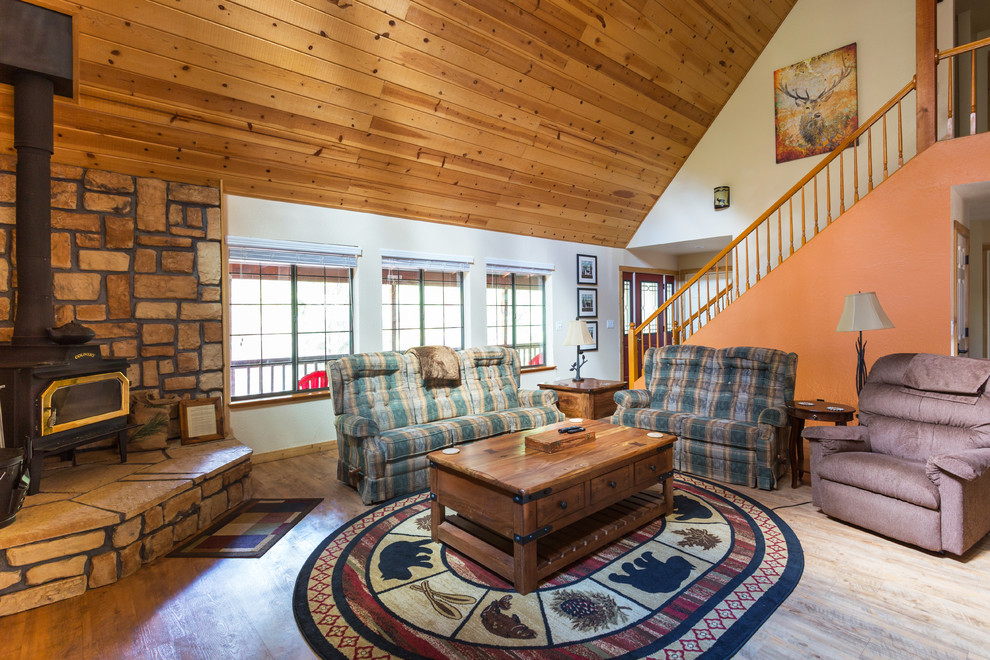 Imagen de salón abierto rural grande con parades naranjas, suelo vinílico, estufa de leña, marco de chimenea de piedra y televisor colgado en la pared