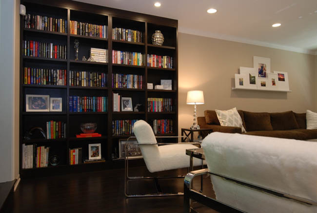 Ejemplo de biblioteca en casa abierta actual de tamaño medio con paredes beige y suelo de madera oscura