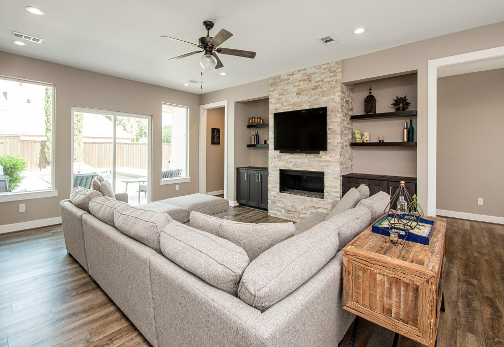 Photo of a medium sized traditional open plan living room in Dallas with beige walls, vinyl flooring, a hanging fireplace, a stone fireplace surround, a wall mounted tv and brown floors.