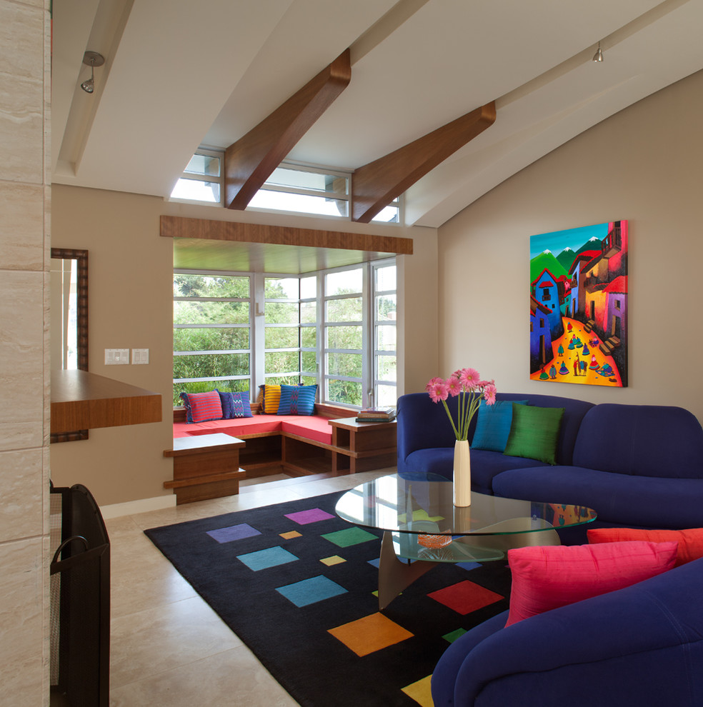 На фото: большая открытая гостиная комната в современном стиле с с книжными шкафами и полками, бежевыми стенами, полом из керамогранита, стандартным камином, фасадом камина из плитки и синим диваном