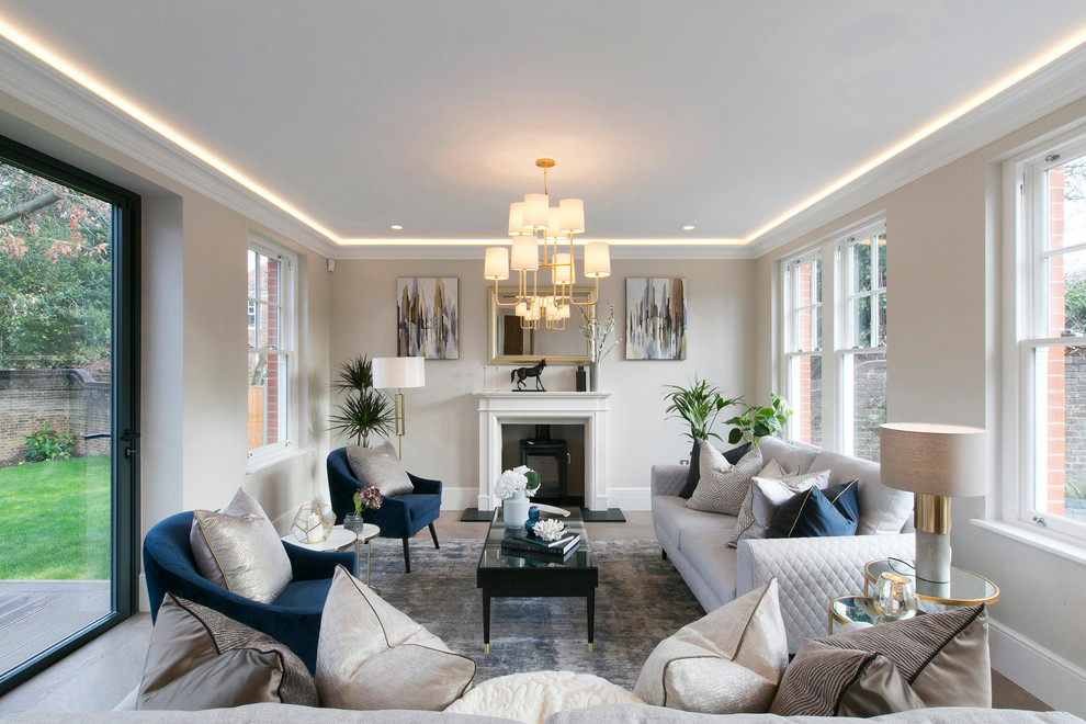 Aménagement d'un grand salon classique avec un mur beige, parquet clair, un poêle à bois, un sol beige et éclairage.