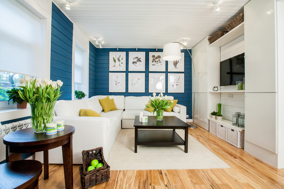 Aménagement d'un salon bord de mer ouvert avec une salle de réception, un mur bleu, parquet clair et un téléviseur fixé au mur.