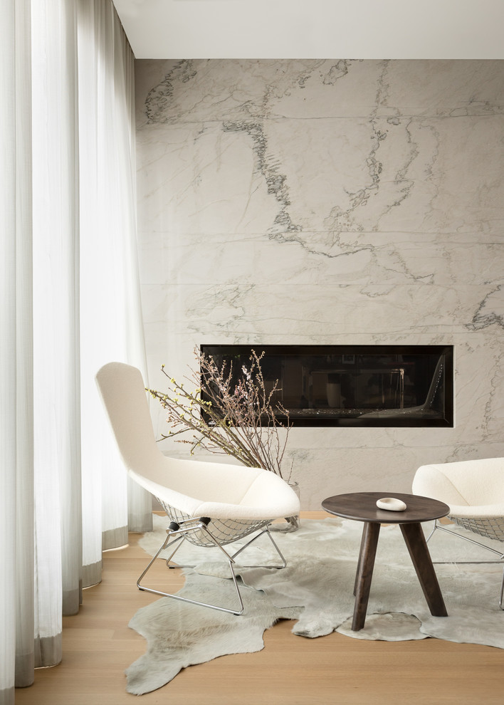 Cette image montre un salon design avec un mur blanc, parquet clair, une cheminée ribbon, un manteau de cheminée en pierre et un sol marron.