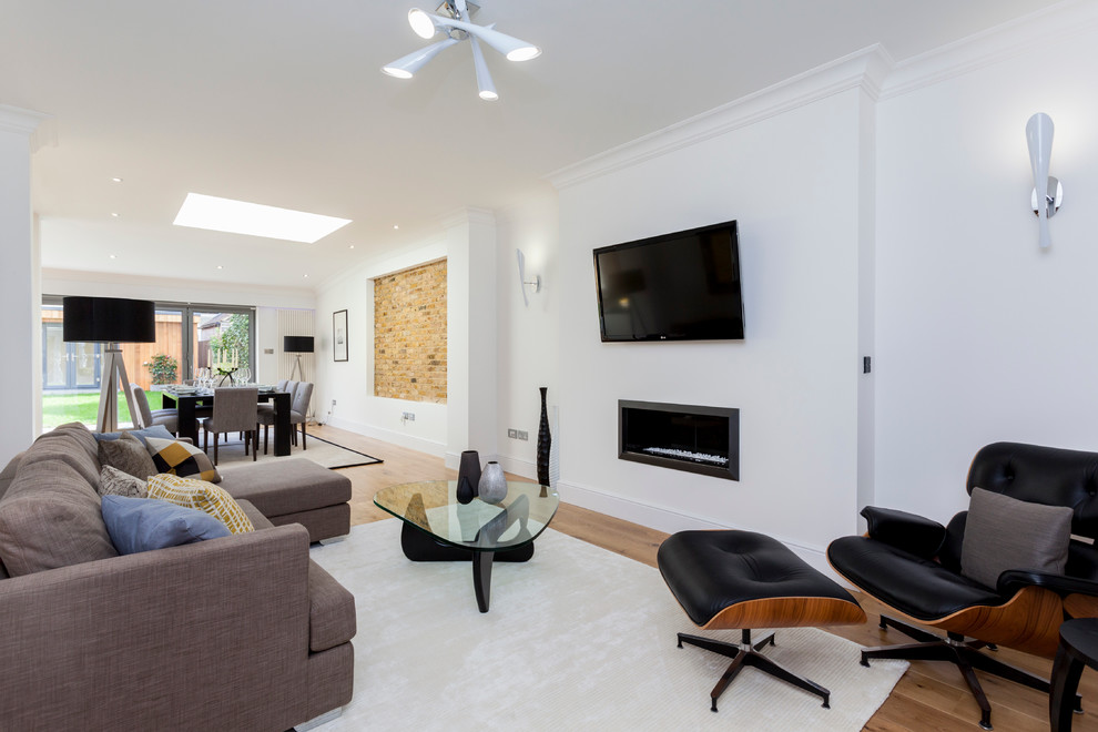 This is an example of a traditional open plan living room in London with white walls, light hardwood flooring, a ribbon fireplace and a wall mounted tv.